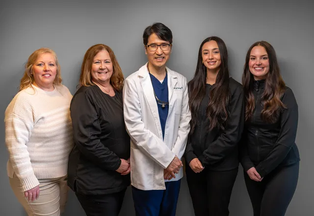 Dental office team of five standing together for a group headshot on a grey backdrop