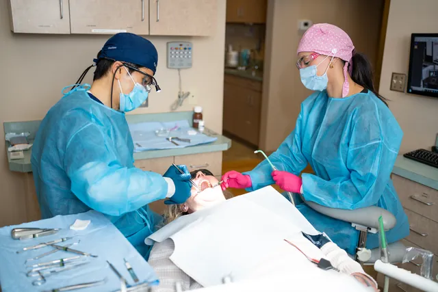 Dentist and assistant in blue gowns and masks treating a patient in the operatory