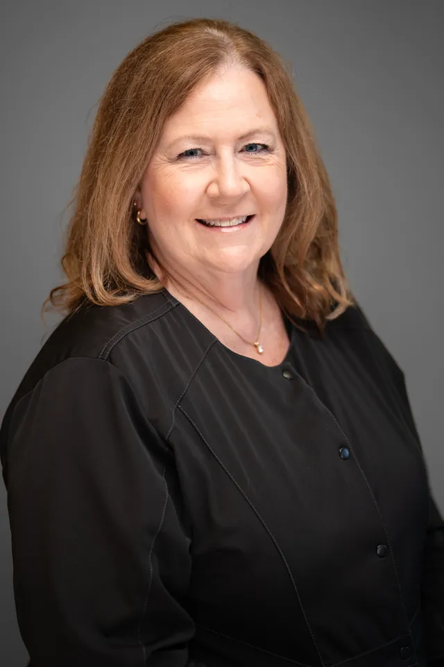 Dental team member in black scrubs smiling for a studio headshot on a grey backdrop