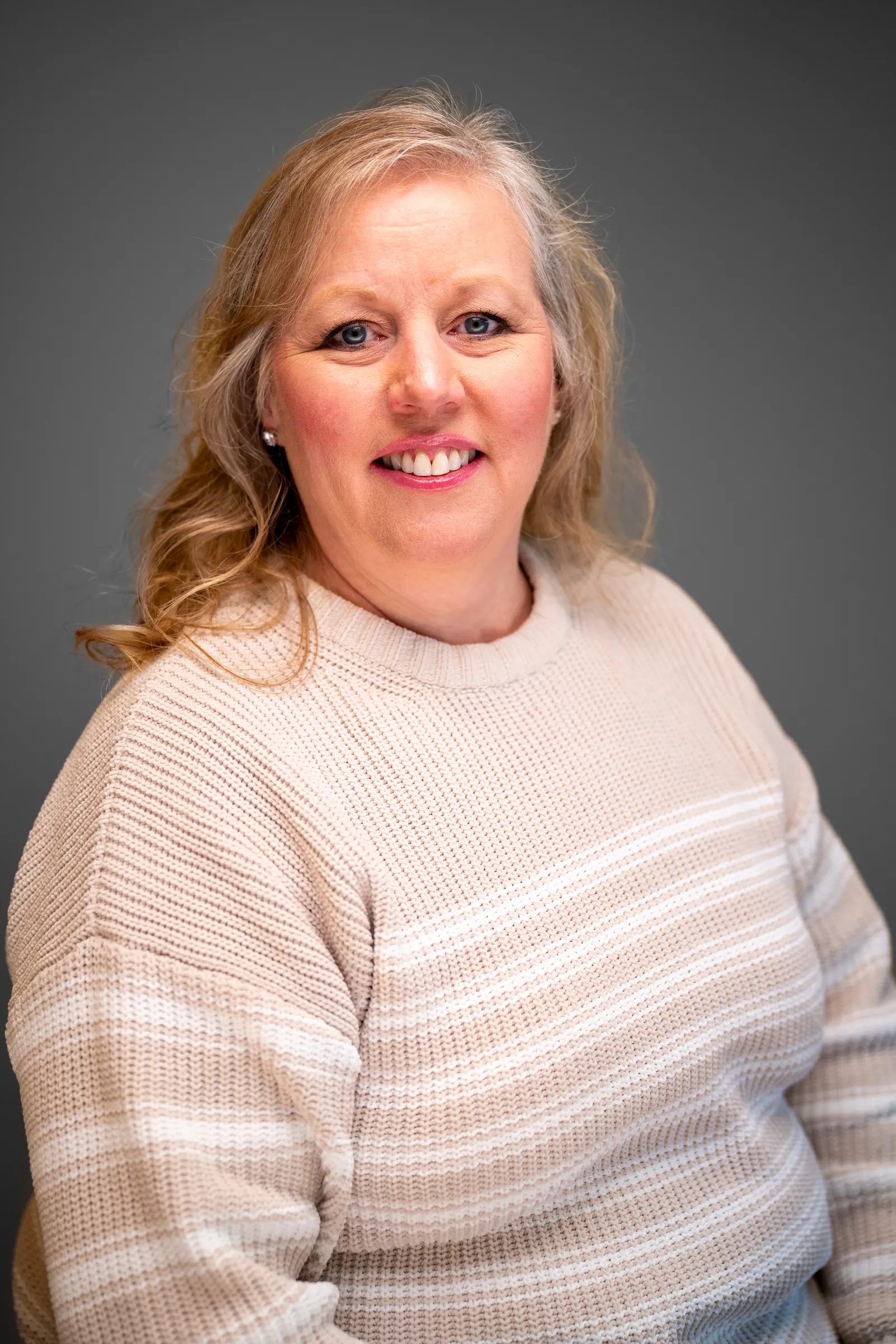 Dental office team member in a striped sweater smiling for a headshot on a grey backdrop