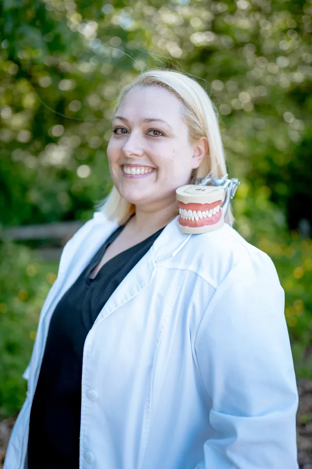 Dentist in a white coat laughing outdoors while holding a dental model