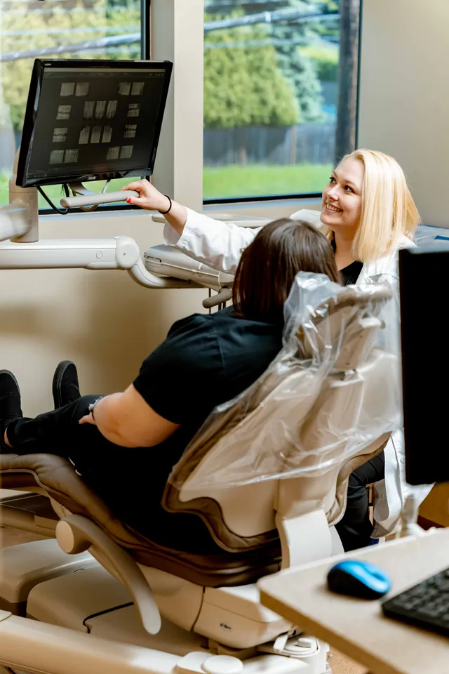 Dentist pointing to an x-ray on a monitor while the patient looks on from the chair