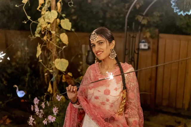 Woman in a blush pink embroidered suit holding a sparkler on Diwali night