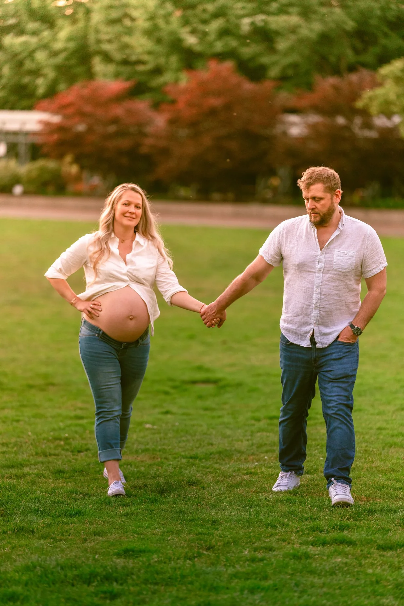 Expecting couple holding hands walking through the park at golden hour
