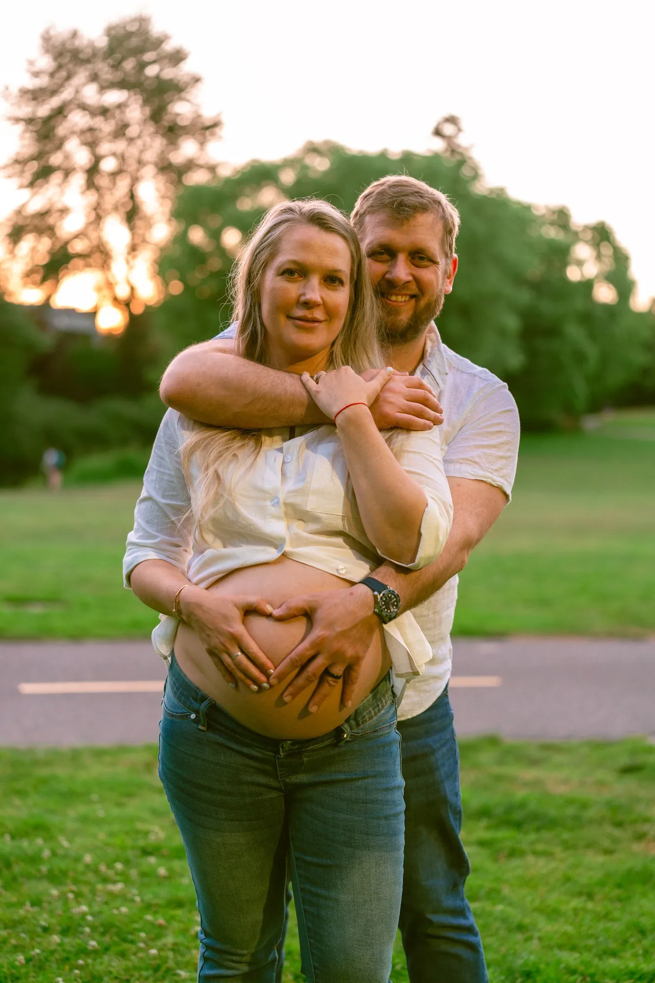 Couple forming a heart with their hands on the baby bump at sunset