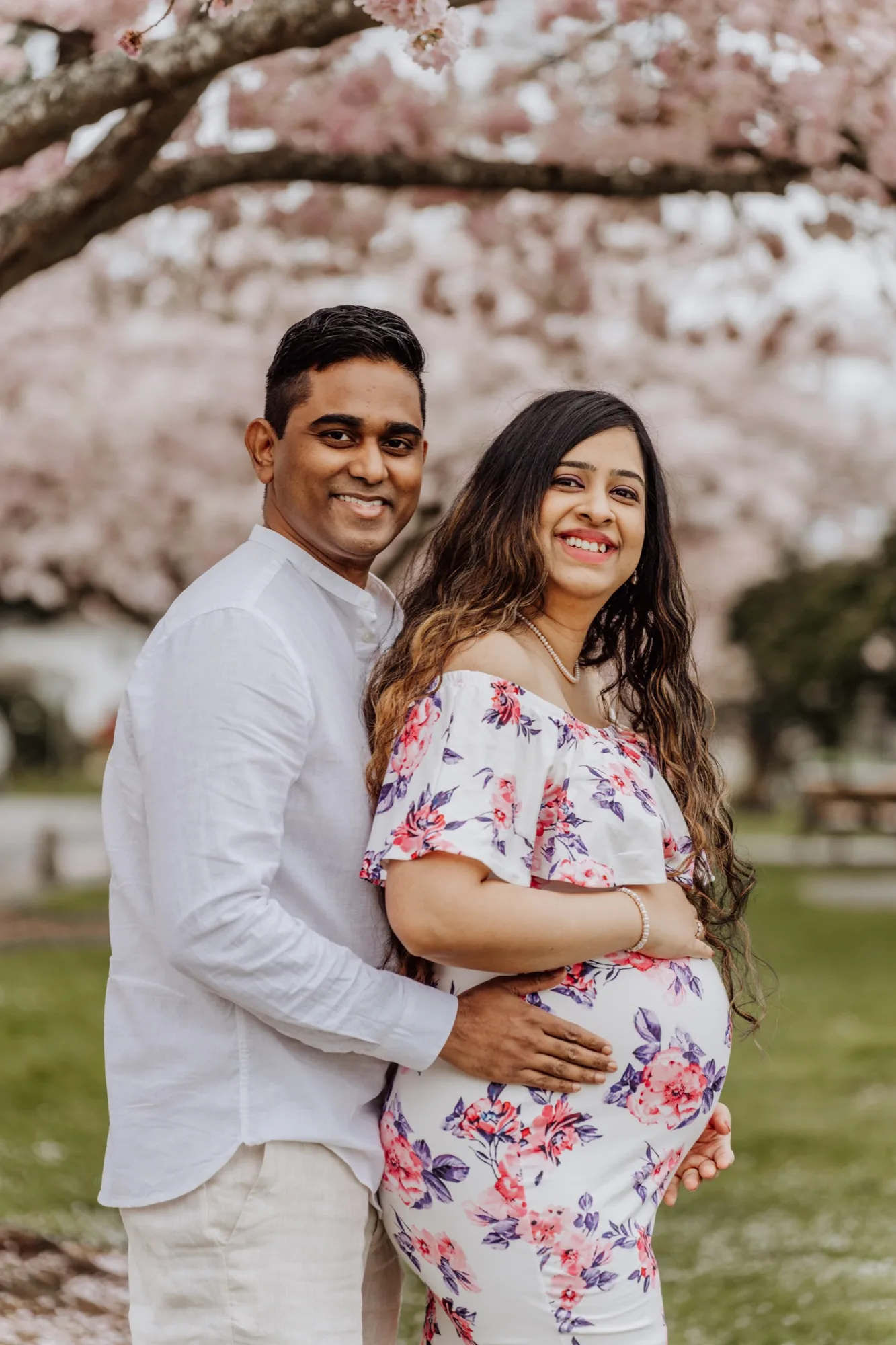 Maternity couple embracing under cherry blossoms in spring