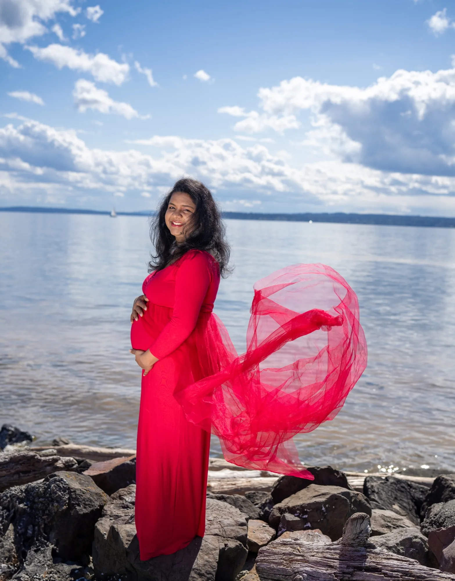Expecting mother in flowing red dress at Mukilteo waterfront rocks maternity session