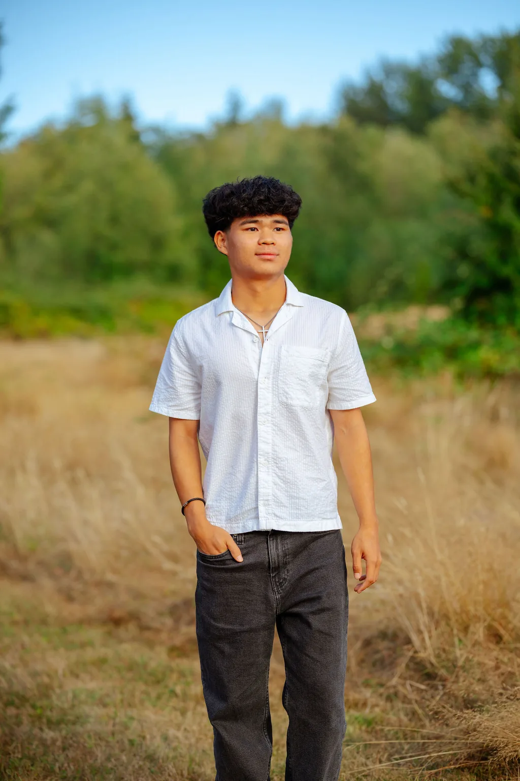 Senior in a white shirt in tall golden grass with evergreens in Lake Stevens under a clear sky