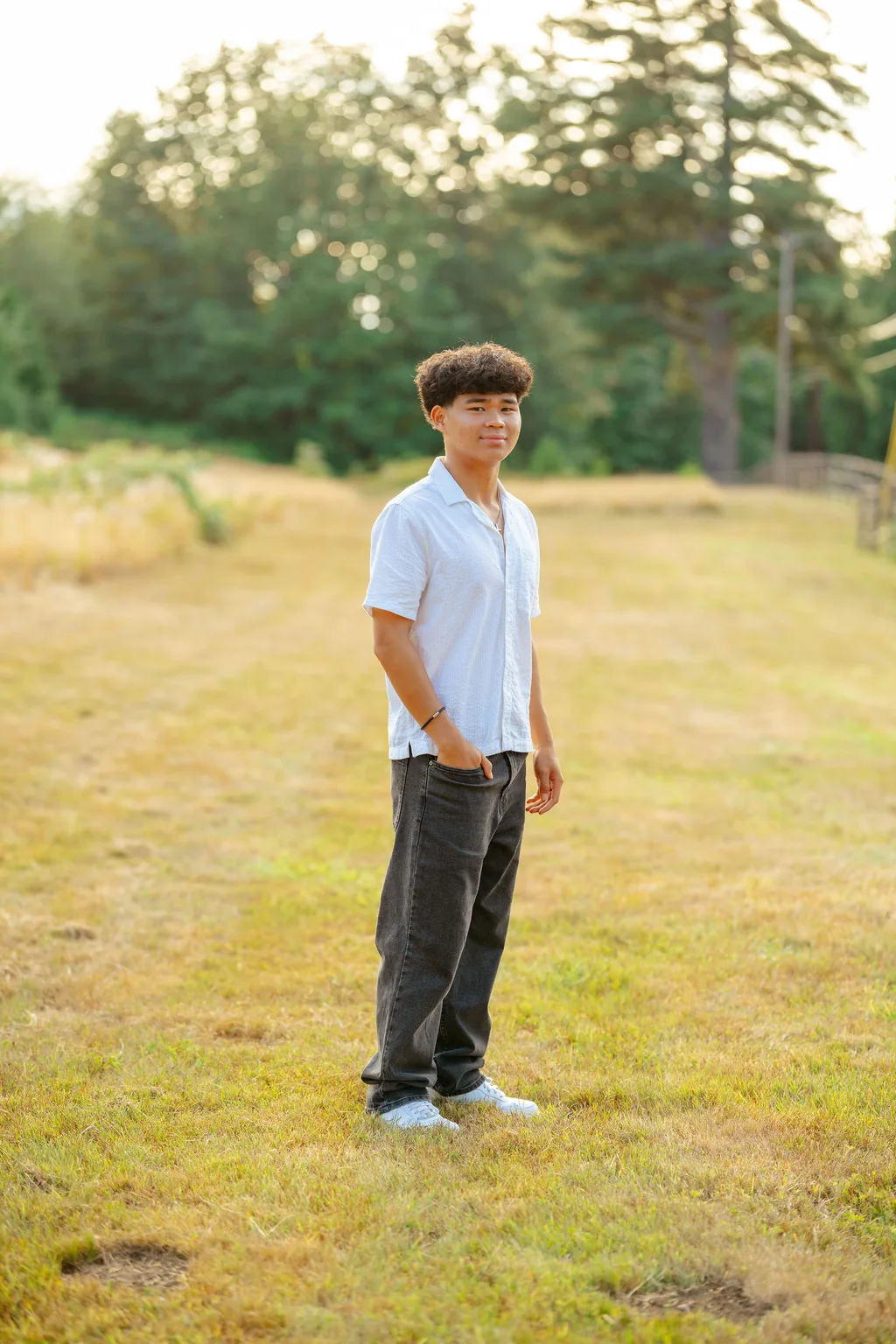 Senior in a white shirt in a dry grass field with evergreens behind him in low sun in Lake Stevens