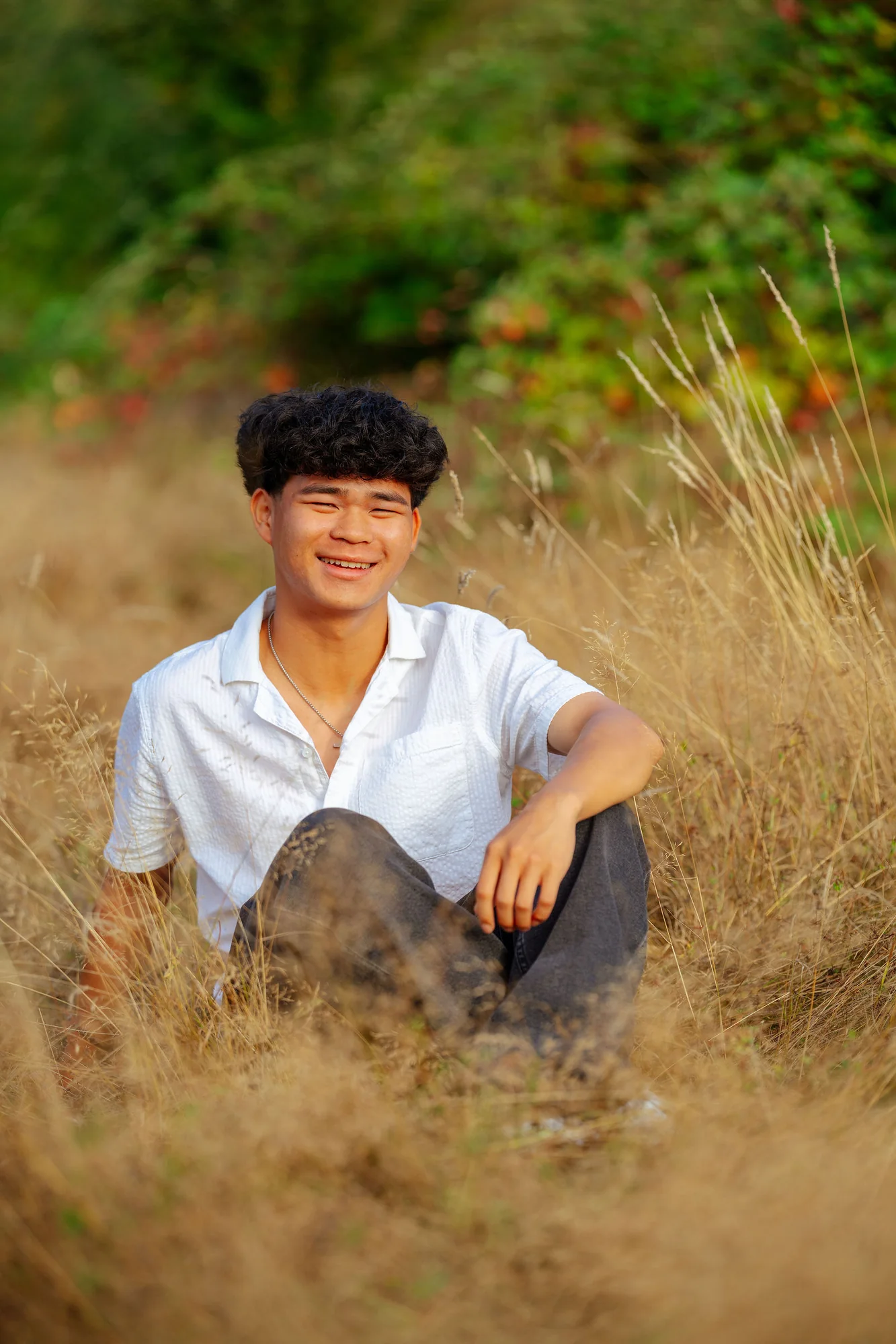 Senior crouching in tall golden grass, smiling at the camera