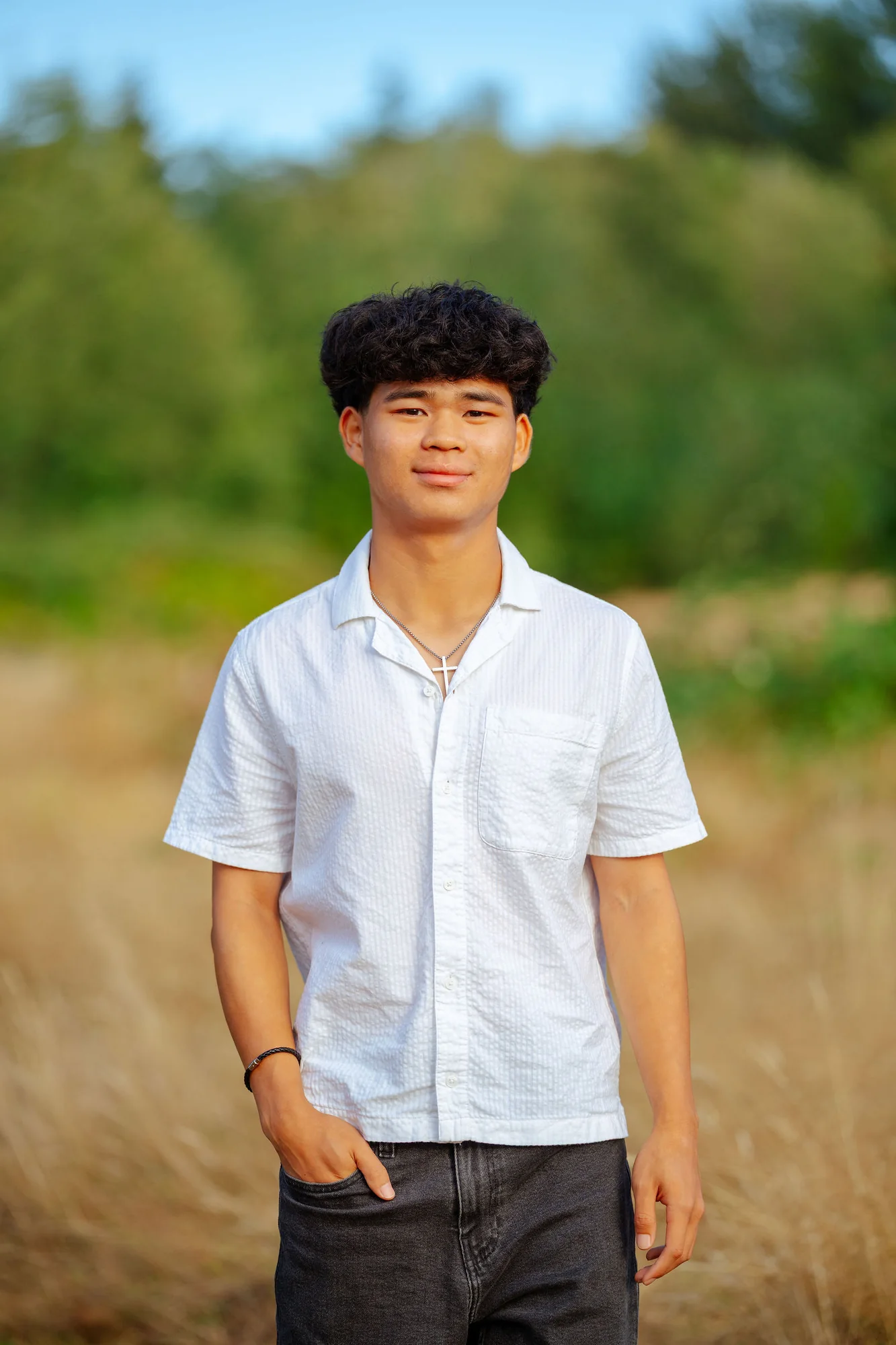Senior in a white shirt standing in a golden field at the end of summer