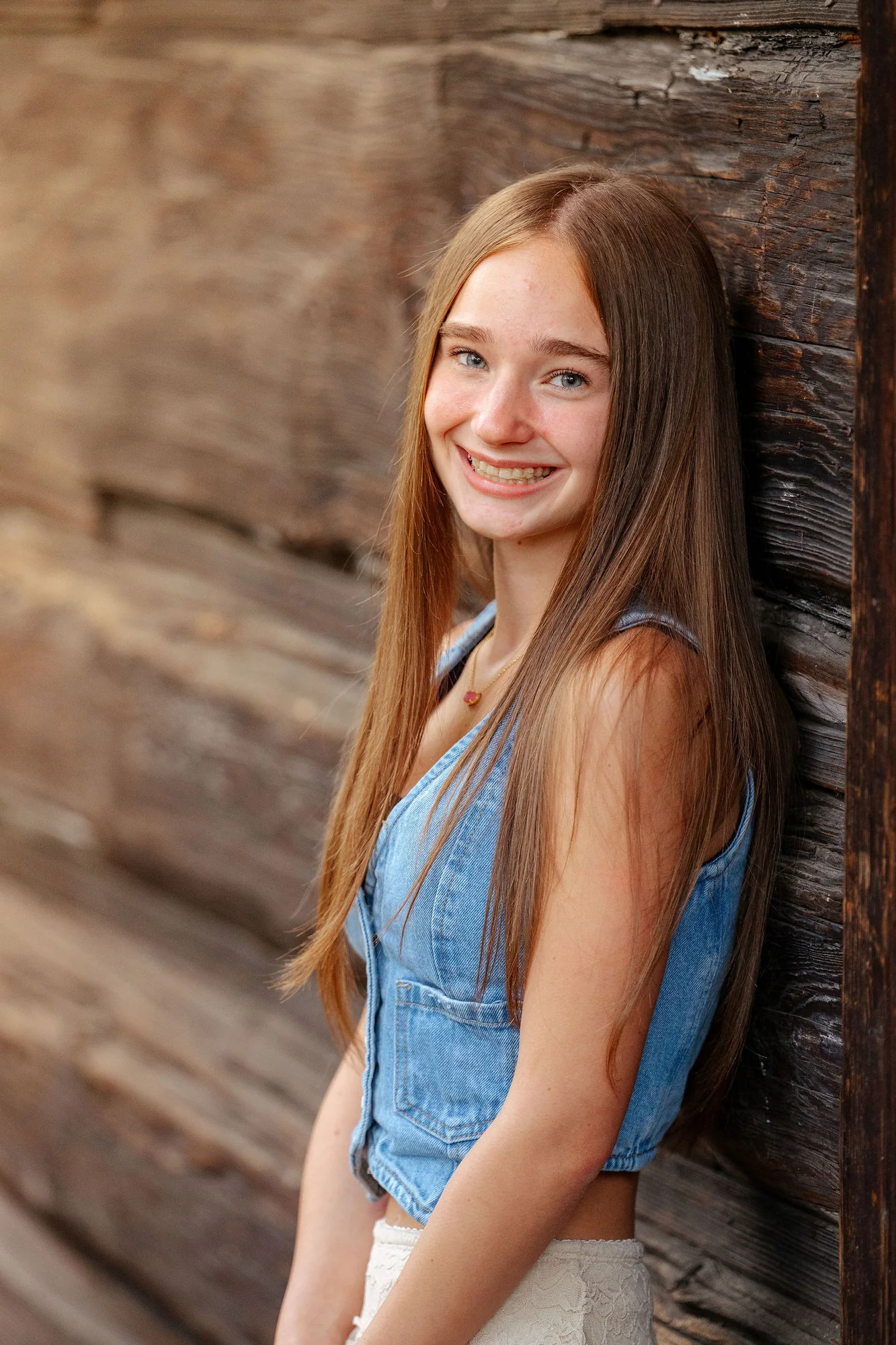 Senior smiling against a weathered barn wall on a summer afternoon