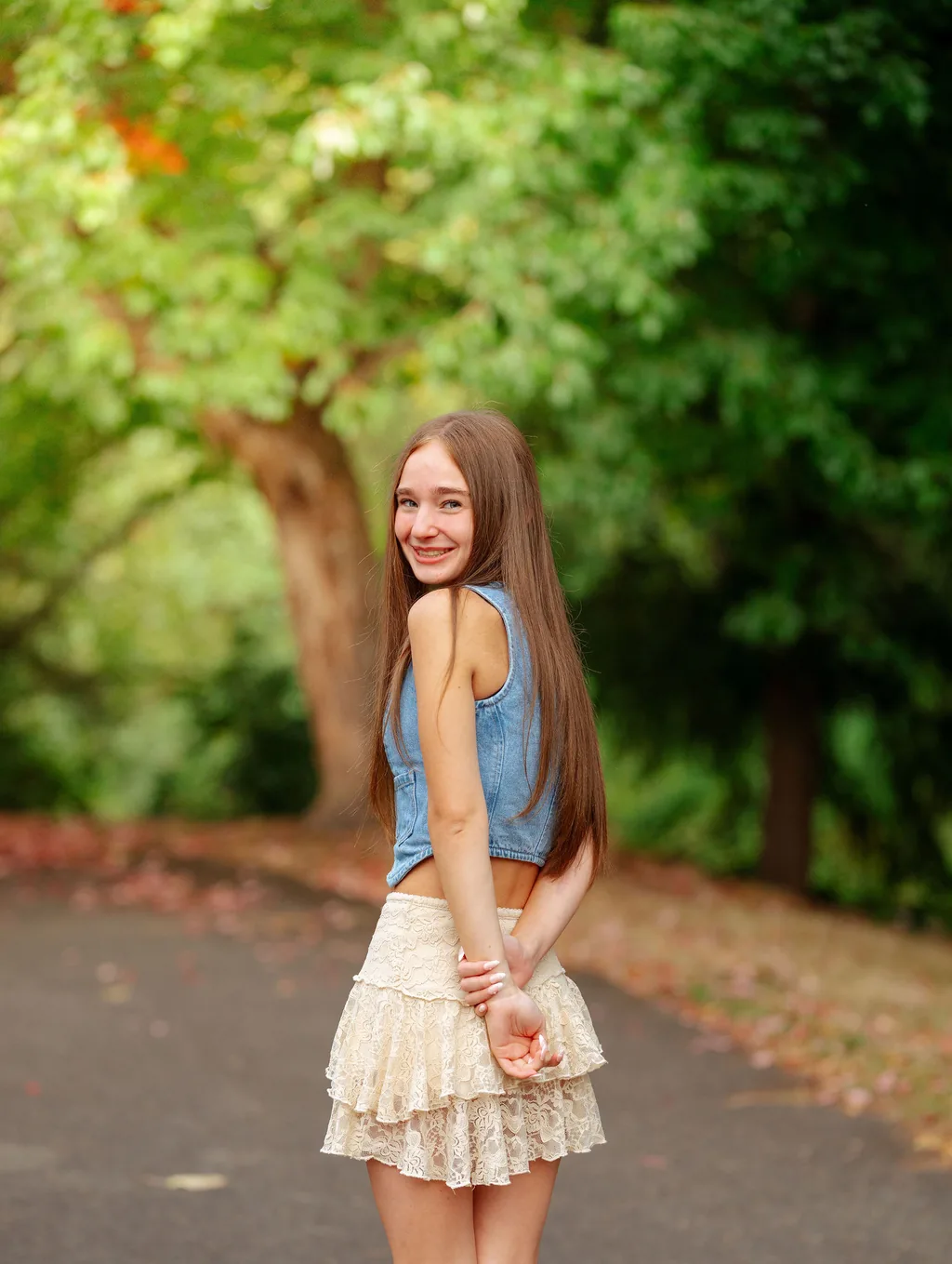 Senior in a denim vest looking back over her shoulder on a tree-lined path in Lake Stevens