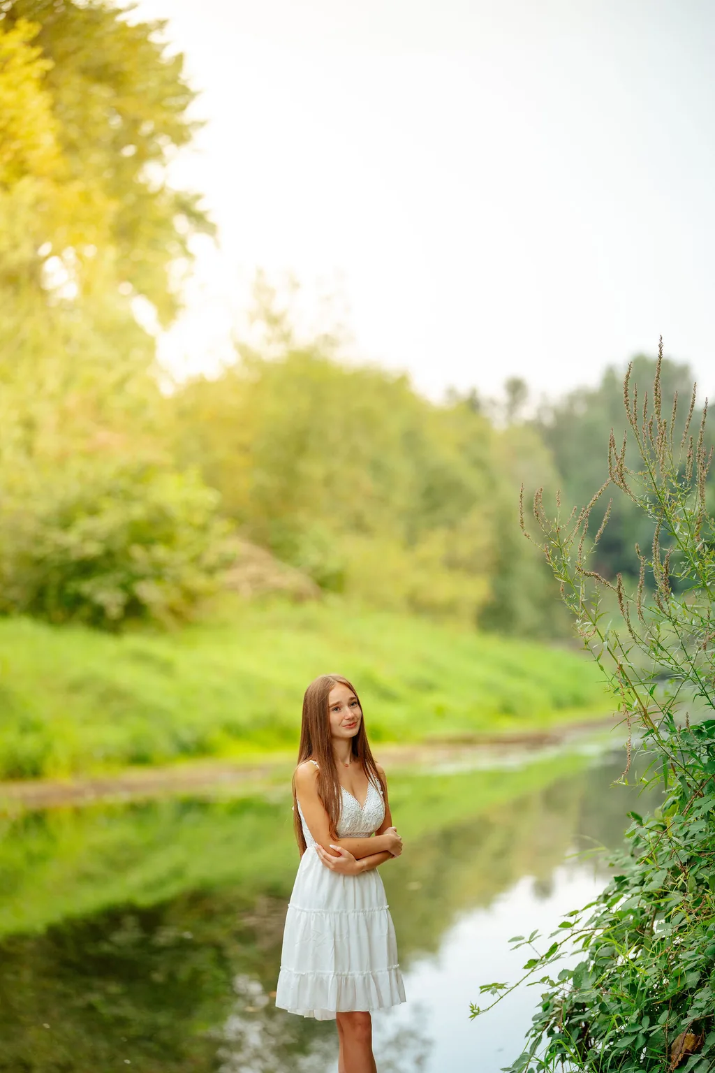 Senior in a white dress beside a still creek in Lake Stevens in soft summer light