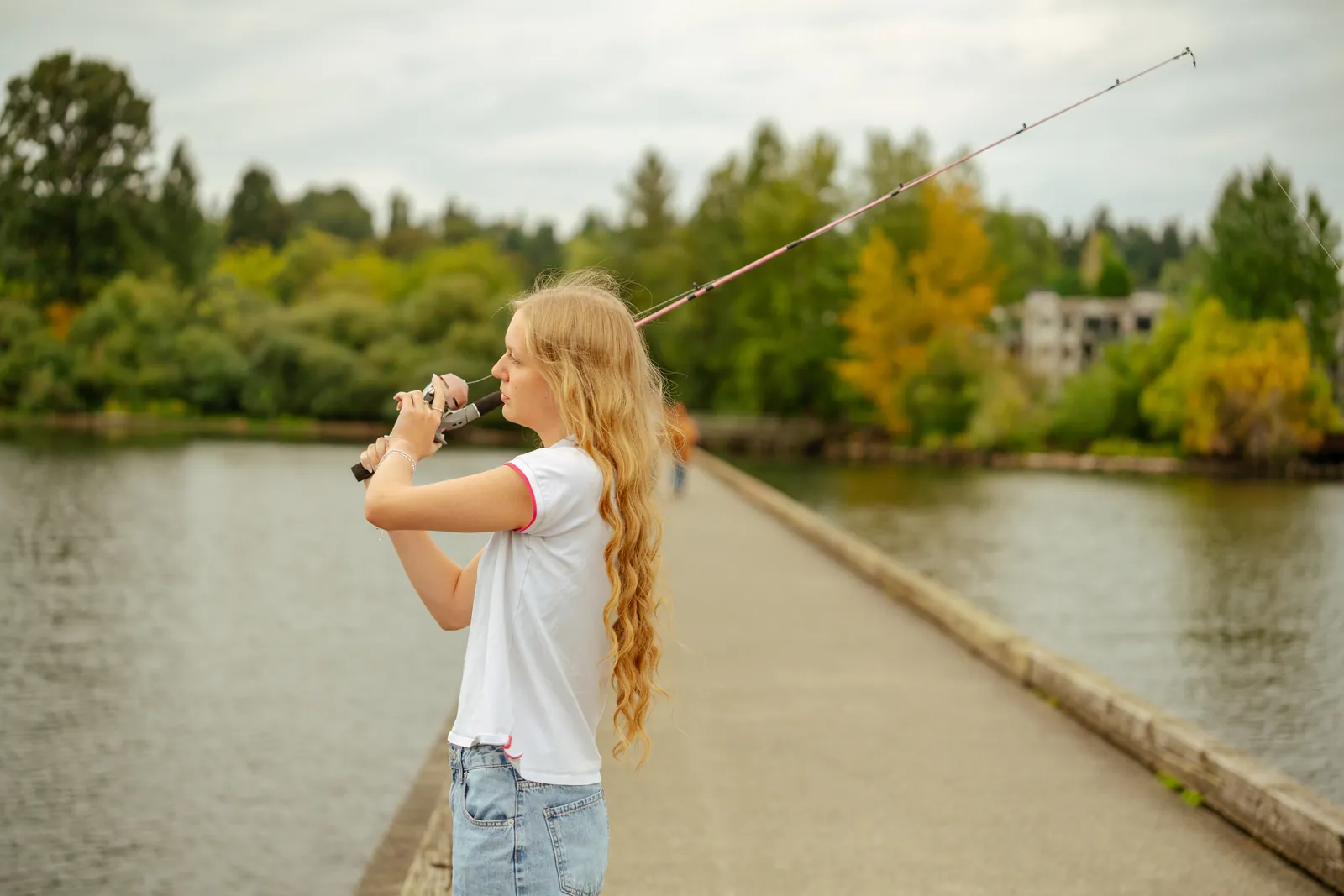 Senior casting a fishing rod from a lakeside boardwalk, trees turning gold across the water