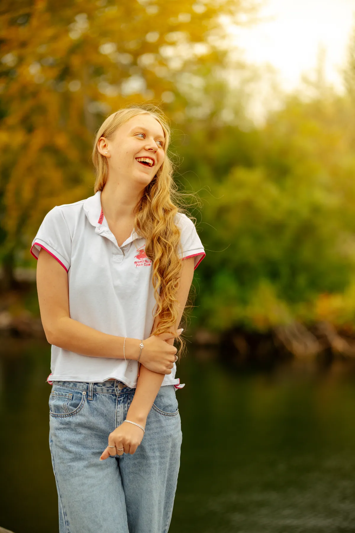 High school senior laughing beside the water in warm evening light