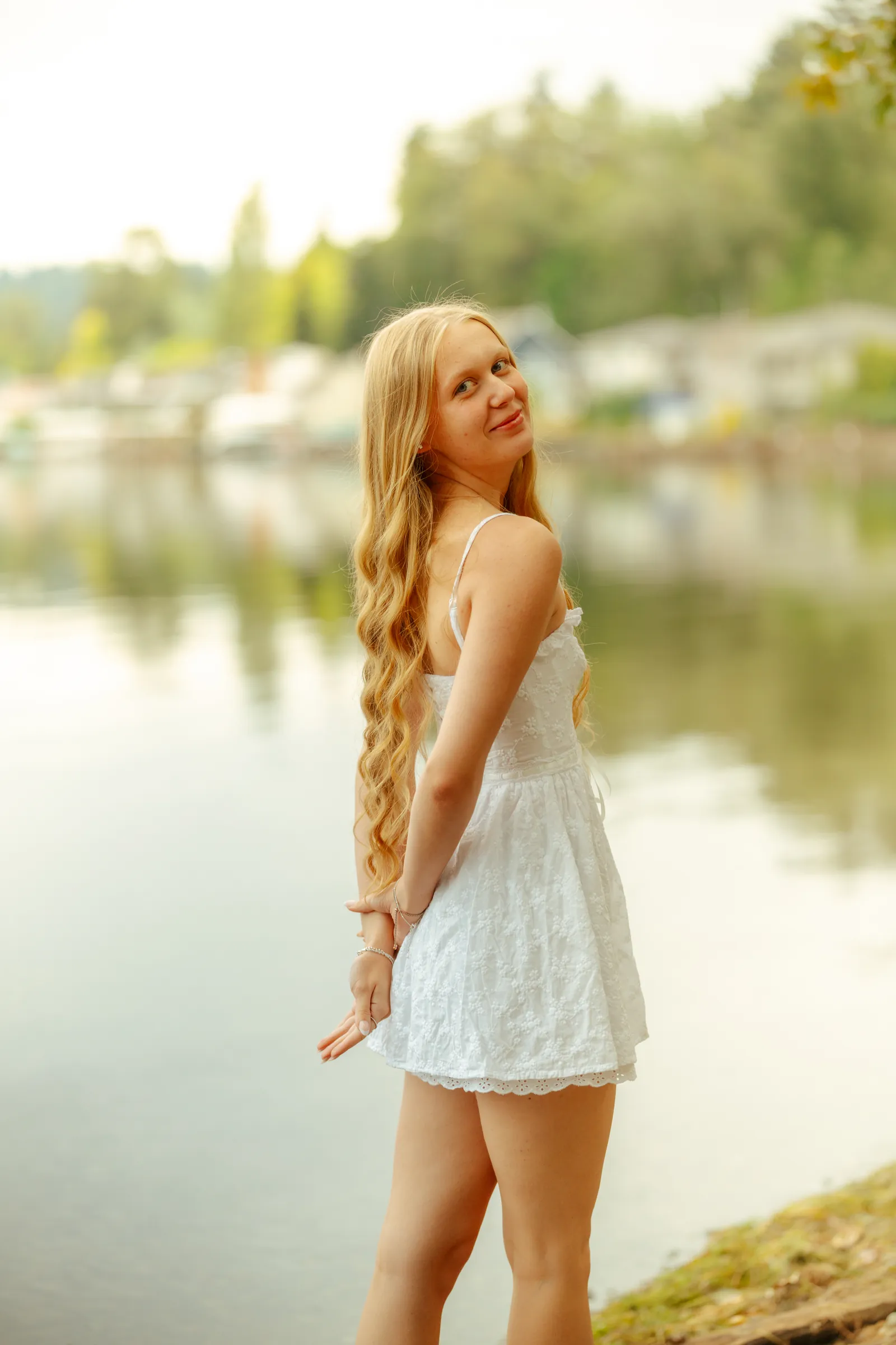 Senior in a white sundress looking back over her shoulder at the lakeshore