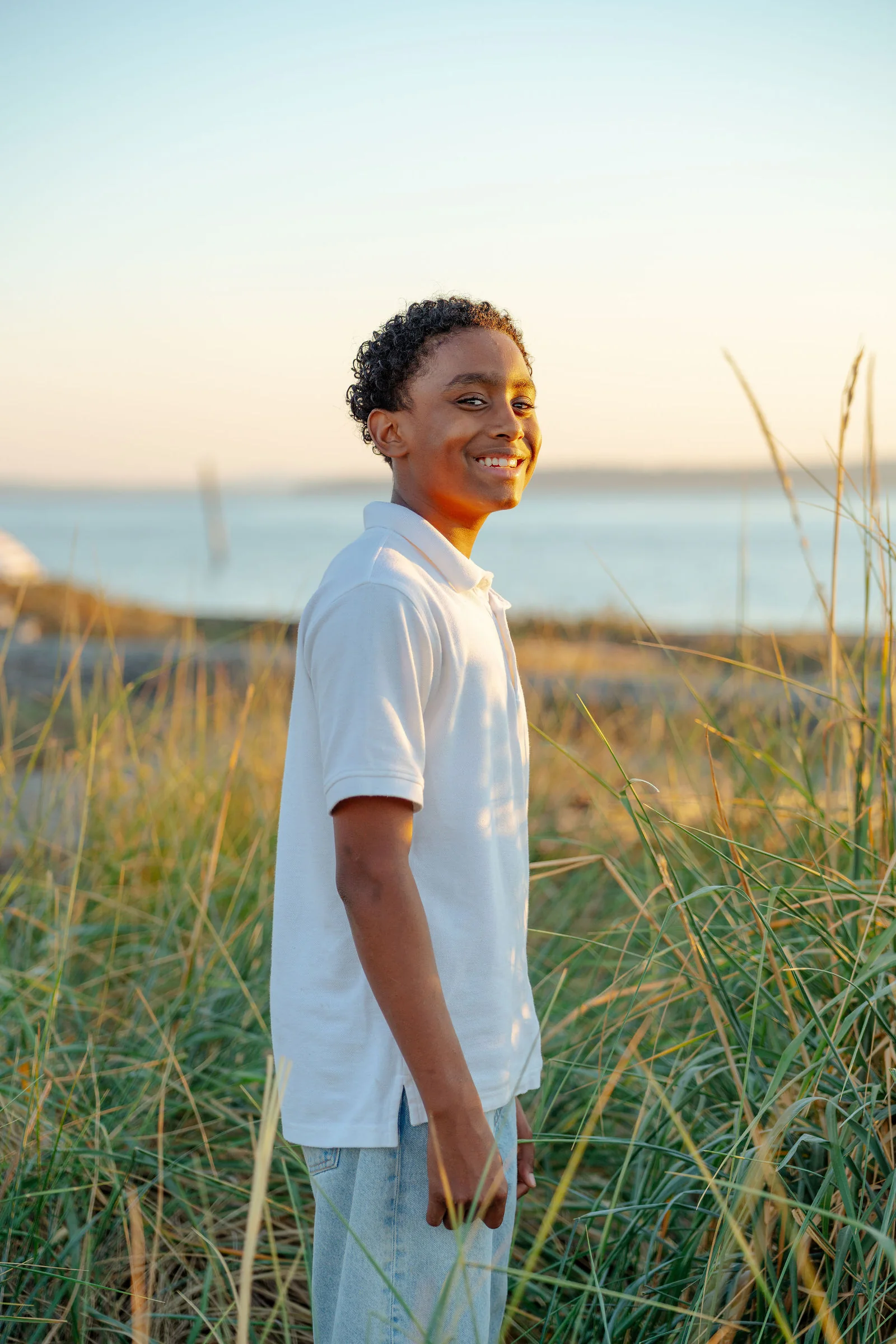Senior in a white polo looking out over the water at sunset
