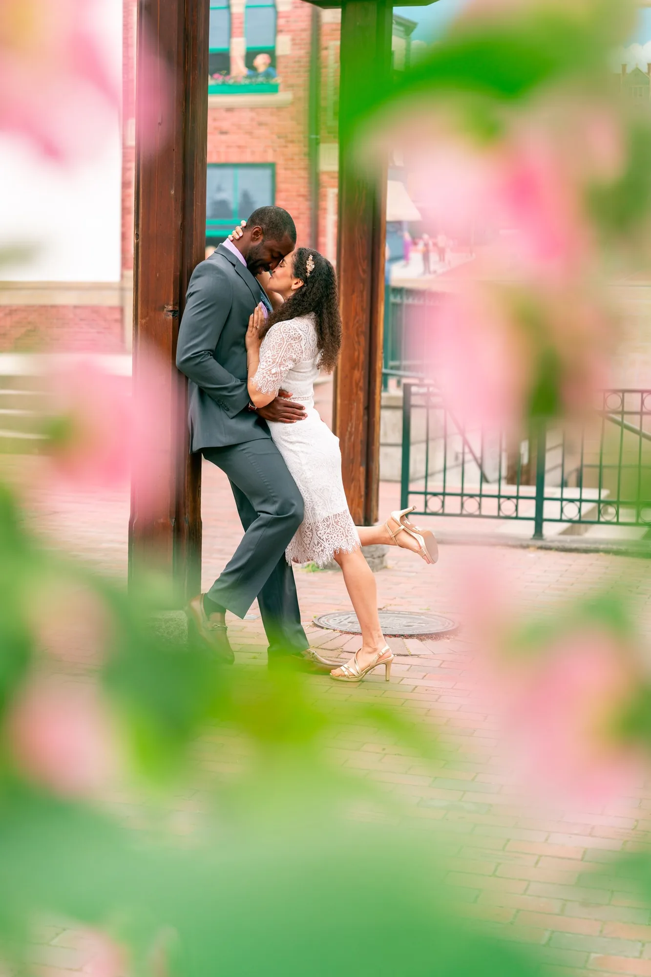 Newlyweds kissing beneath a wooden arbor framed by pink blossoms