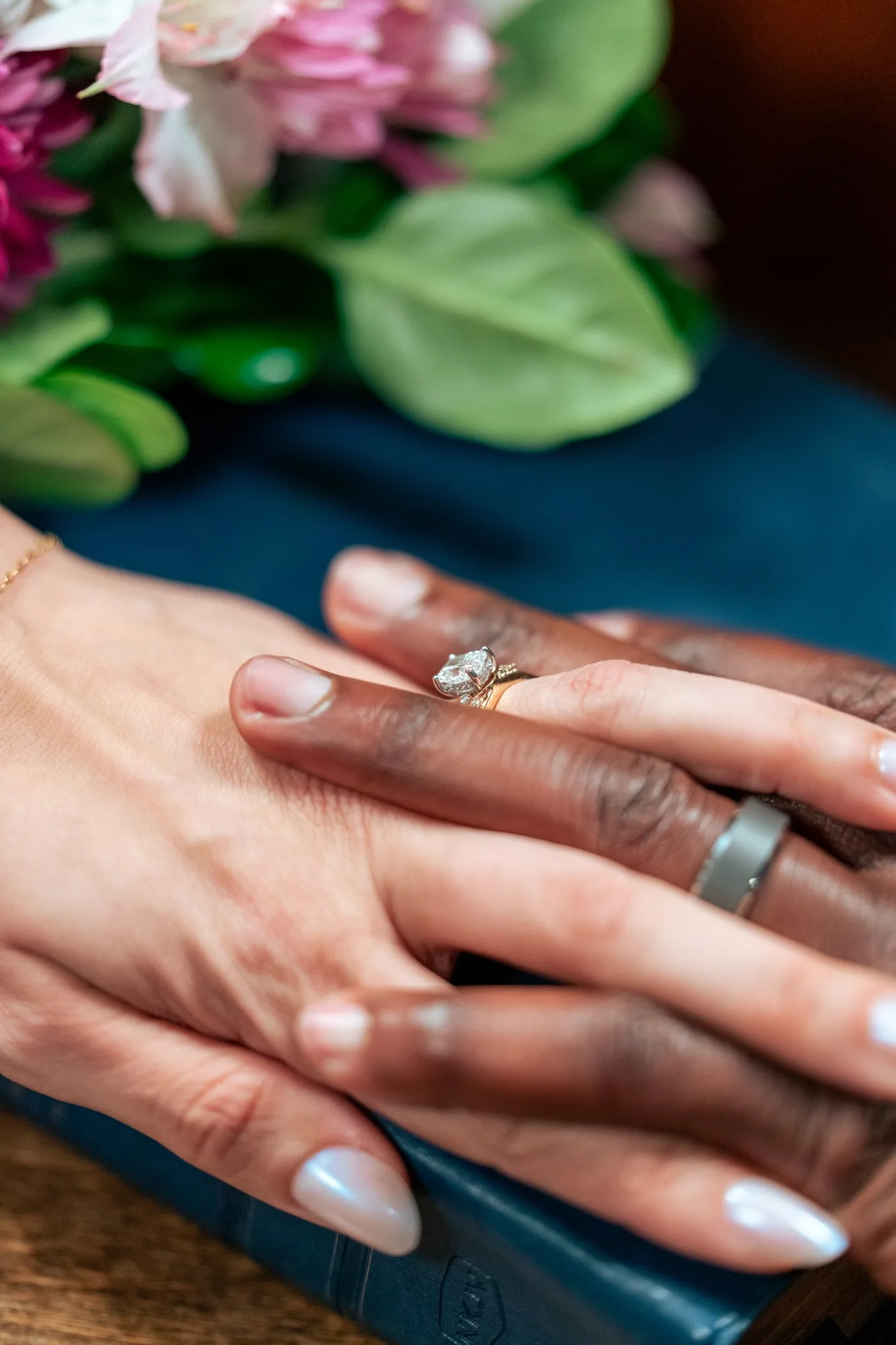 Close-up of the newlyweds' hands showing their wedding rings beside the bouquet