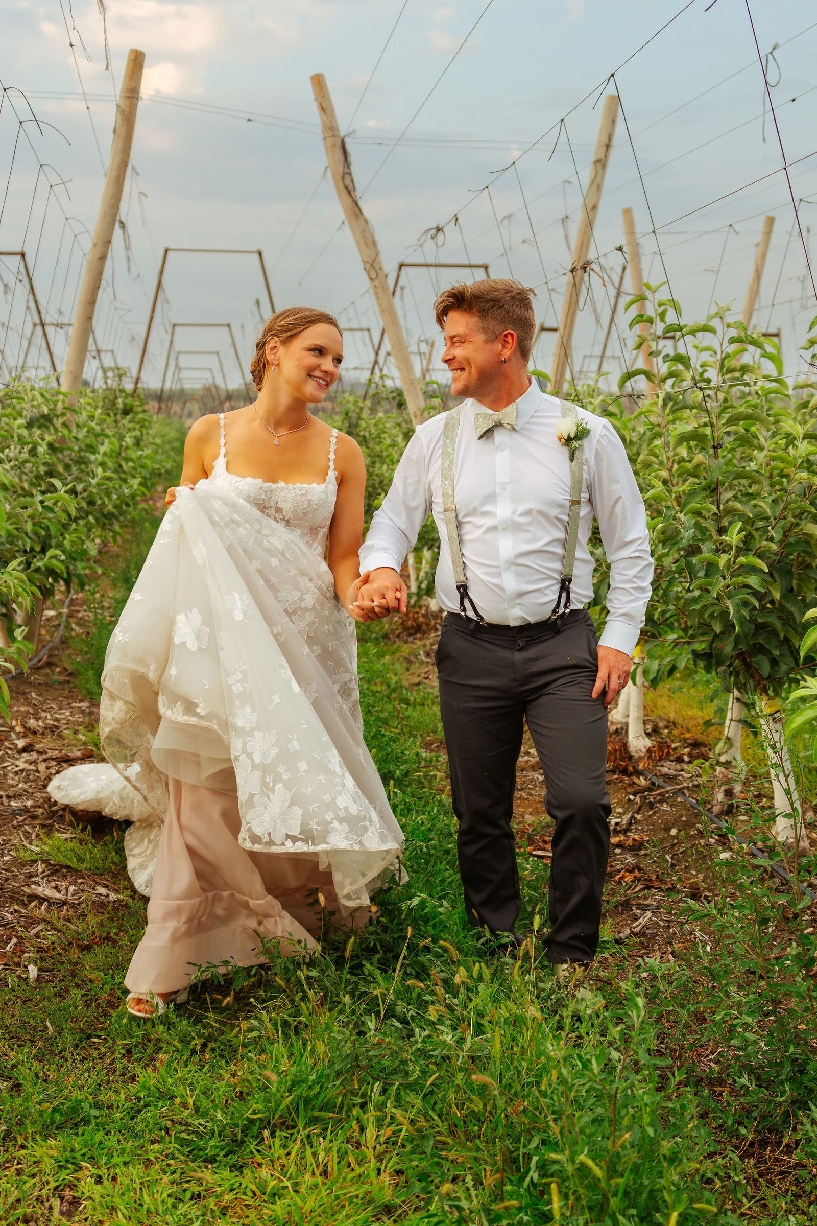 Bride and groom walking through the green orchard together