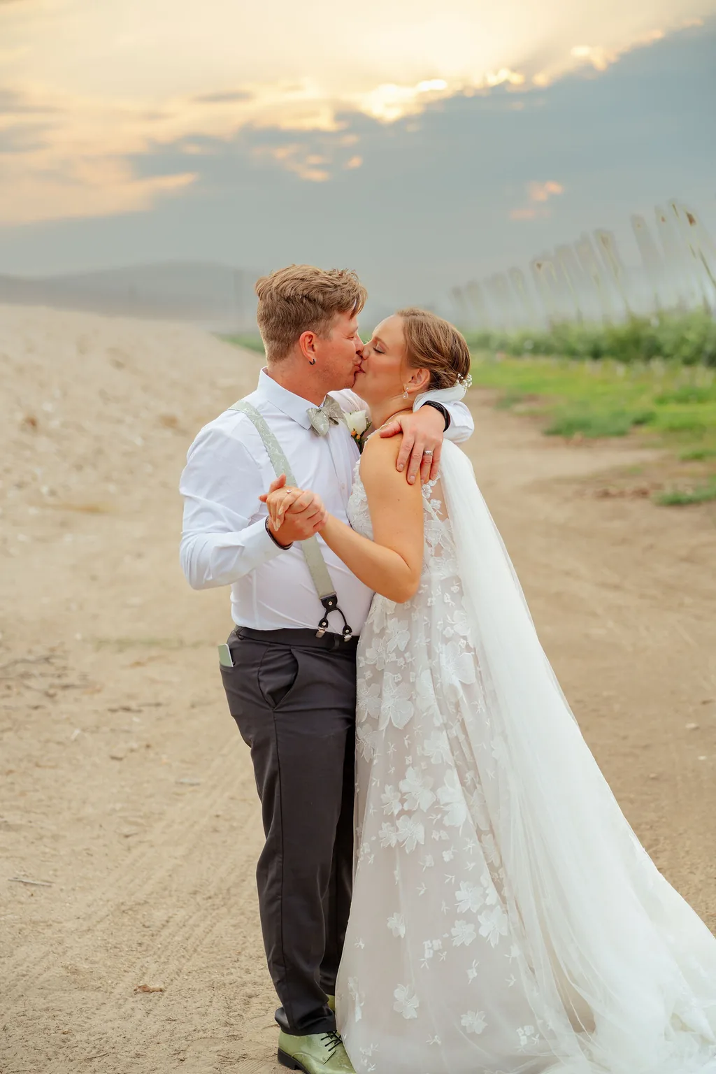 Groom kissing the bride's forehead on a farm road at sunset