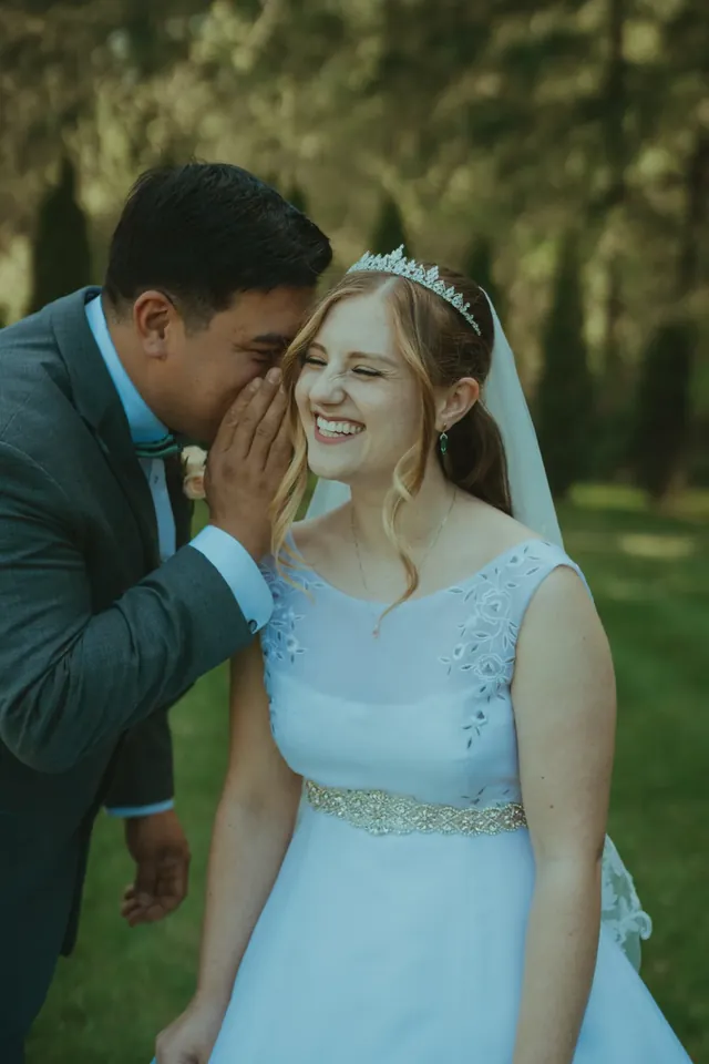 Groom whispering to his laughing bride in a tiara and veil