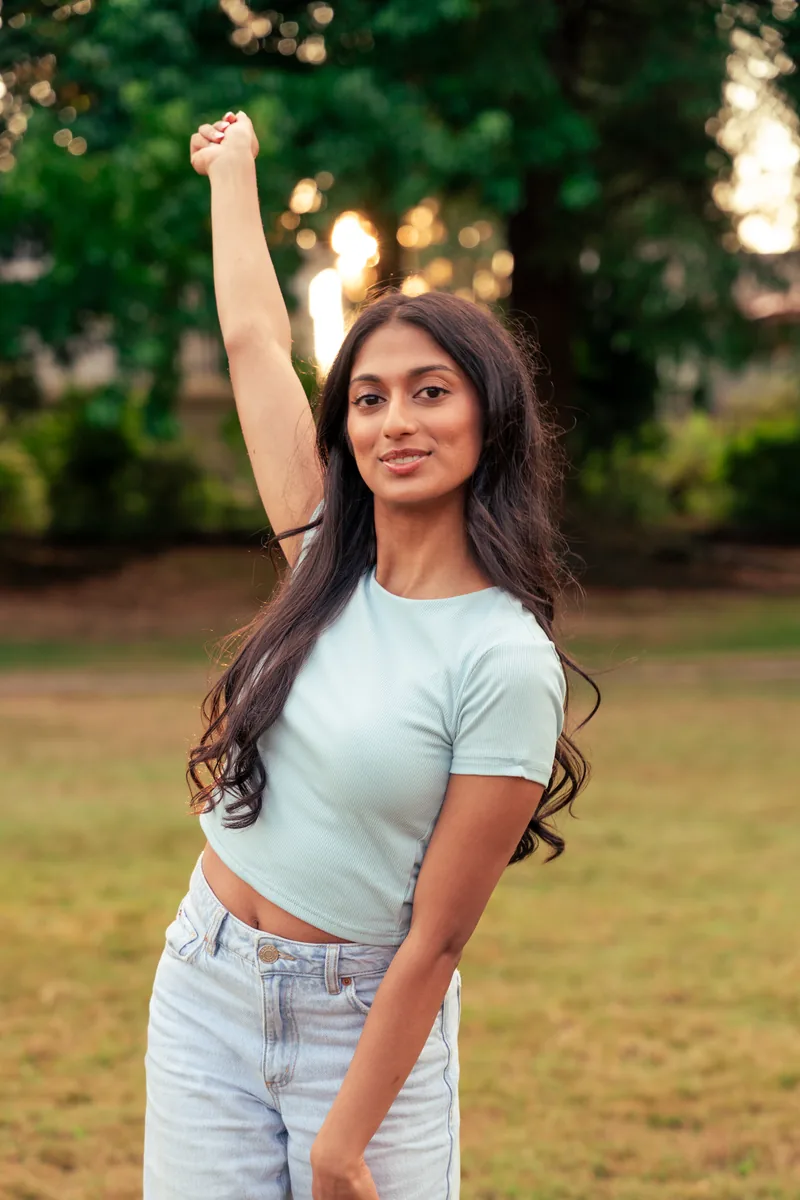 Senior portrait, arm raised, backlit at sunset in the park